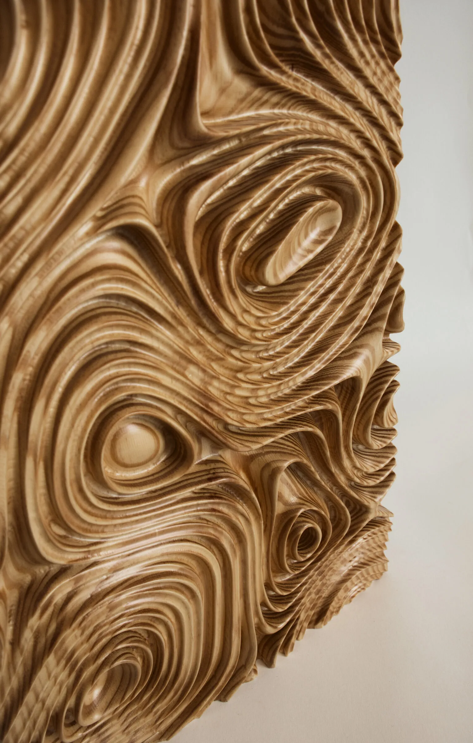A carved wall panel stands outdoors among trees, its wood surface marked by flowing grain.